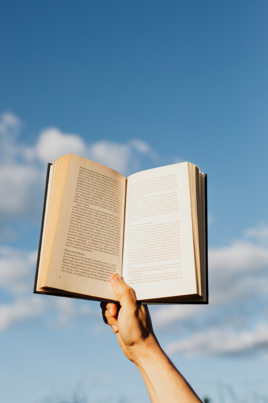 Un livre ouvert tenu à bout de bras contre un ciel bleu
